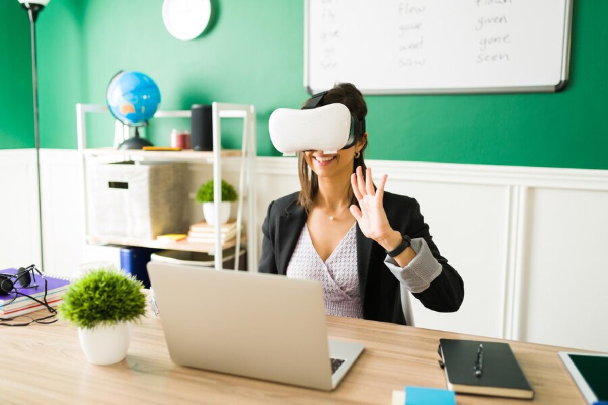 A woman in business attire using a VR headset in a vibrant office, waving her hand with a smile.