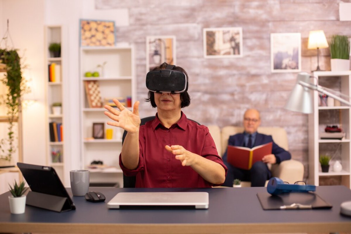 Woman using virtual reality headset in office, with a man reading in background.