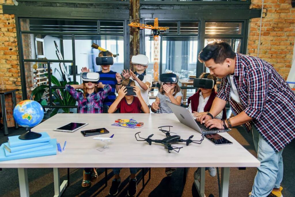 Group of children wearing VR headsets in a classroom as an adult assists with a laptop.