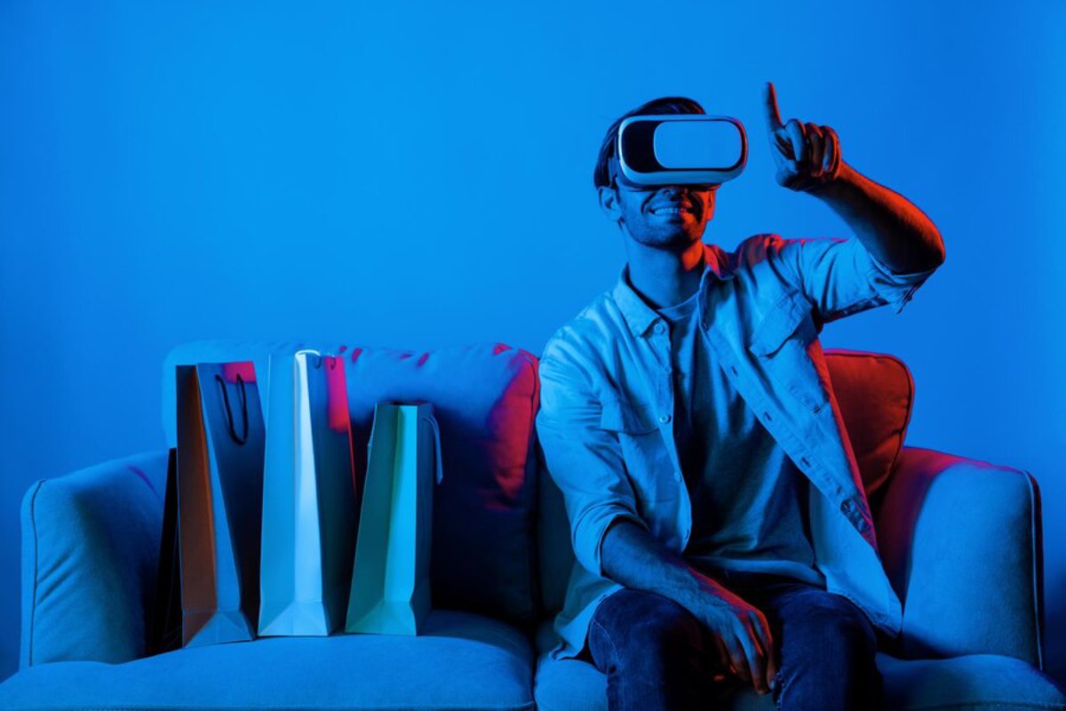 Man using virtual reality headset, sitting on a couch with shopping bags beside him, in a blue-lit room.