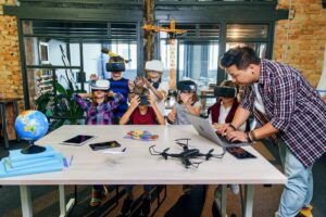 Group of children wearing VR headsets in a classroom as an adult assists with a laptop.