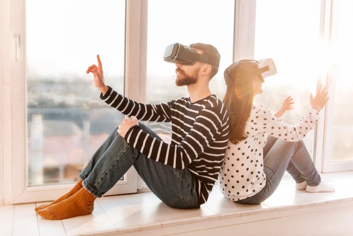 Man and woman sitting on a windowsill, both wearing virtual reality headsets, interacting with unseen content.