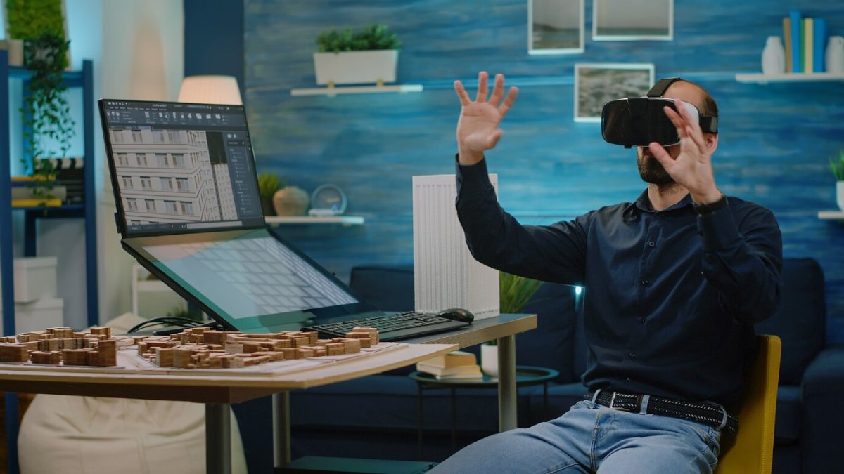 Man wearing virtual reality headset, interacting with digital content in an office filled with technology and architectural models.