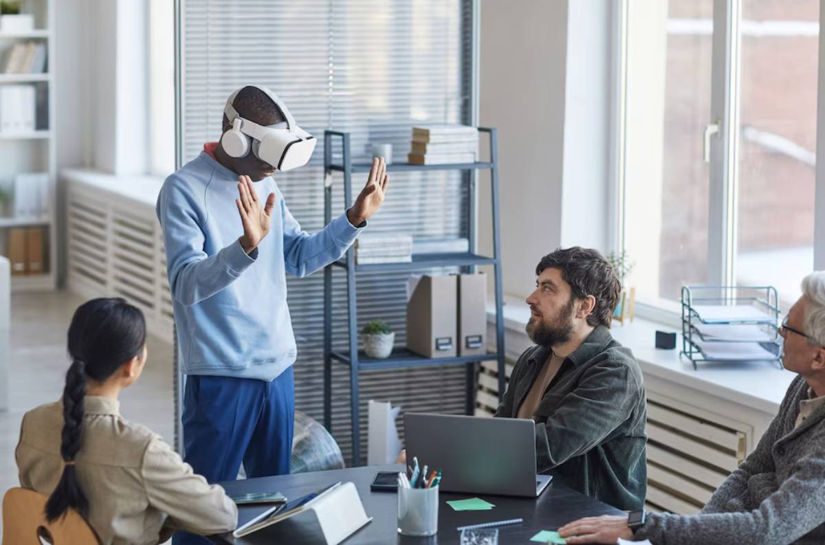 Man wearing VR headset gesturing, with three colleagues observing in a modern office setting.
