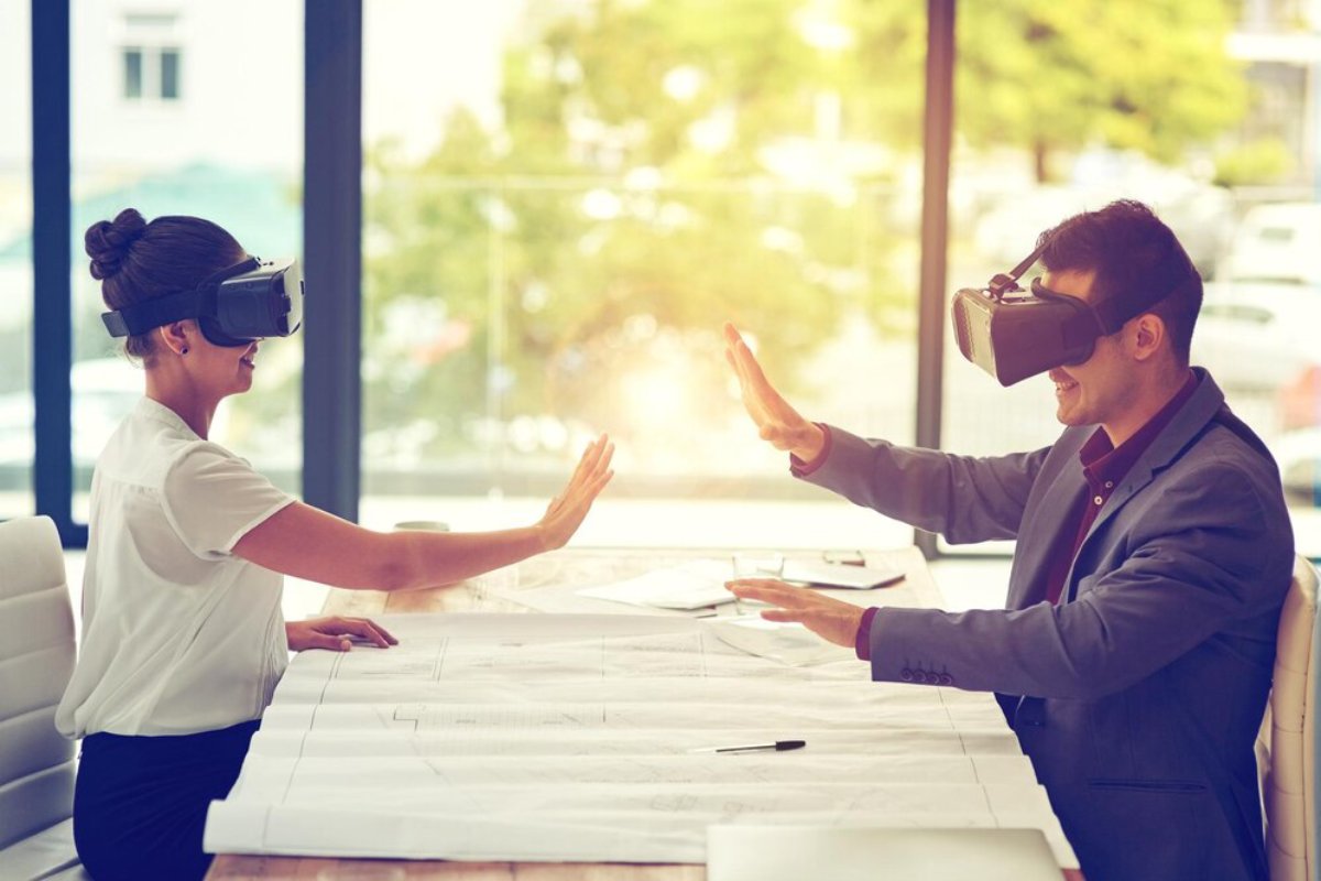 Two professionals wearing virtual reality headsets high-five over blueprints in a bright office.