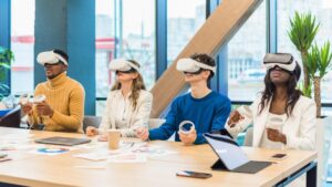Four diverse people use virtual reality headsets in a modern office setting, sitting around a table with technology and documents.