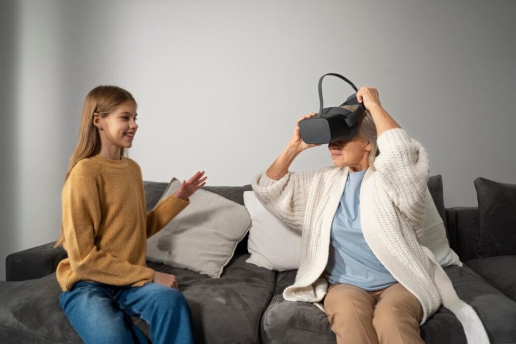 Young woman interacts with an older woman using a virtual reality headset on a couch.