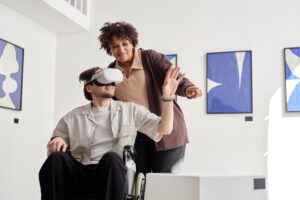Woman assists man in a wheelchair using virtual reality headset in a modern, art-adorned room.