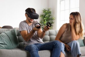 Man enjoys using a VR headset in living room while a woman sits beside him, looking unamused.