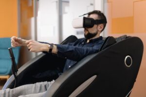 Man wearing VR headset sits in a reclining chair, simulating driving with hands in a bright office setting.