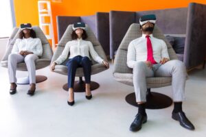 Three professionals sitting in lounge chairs wearing virtual reality headsets in a modern office setting.