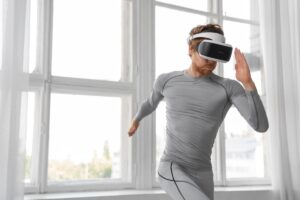 Man in gray athletic wear using a VR headset in a bright room with large windows.