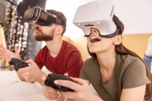 Two people enjoying a virtual reality game, wearing VR headsets and holding controllers, visibly amused.