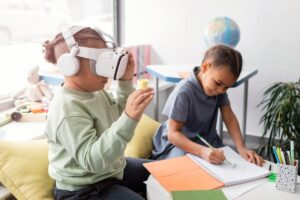 Two children at a study table; one explores with a VR headset while the other draws in a notebook.