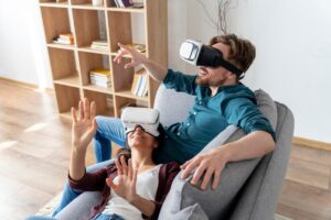 A man and a woman wearing virtual reality headsets, enthusiastically exploring digital worlds while sitting on a couch.